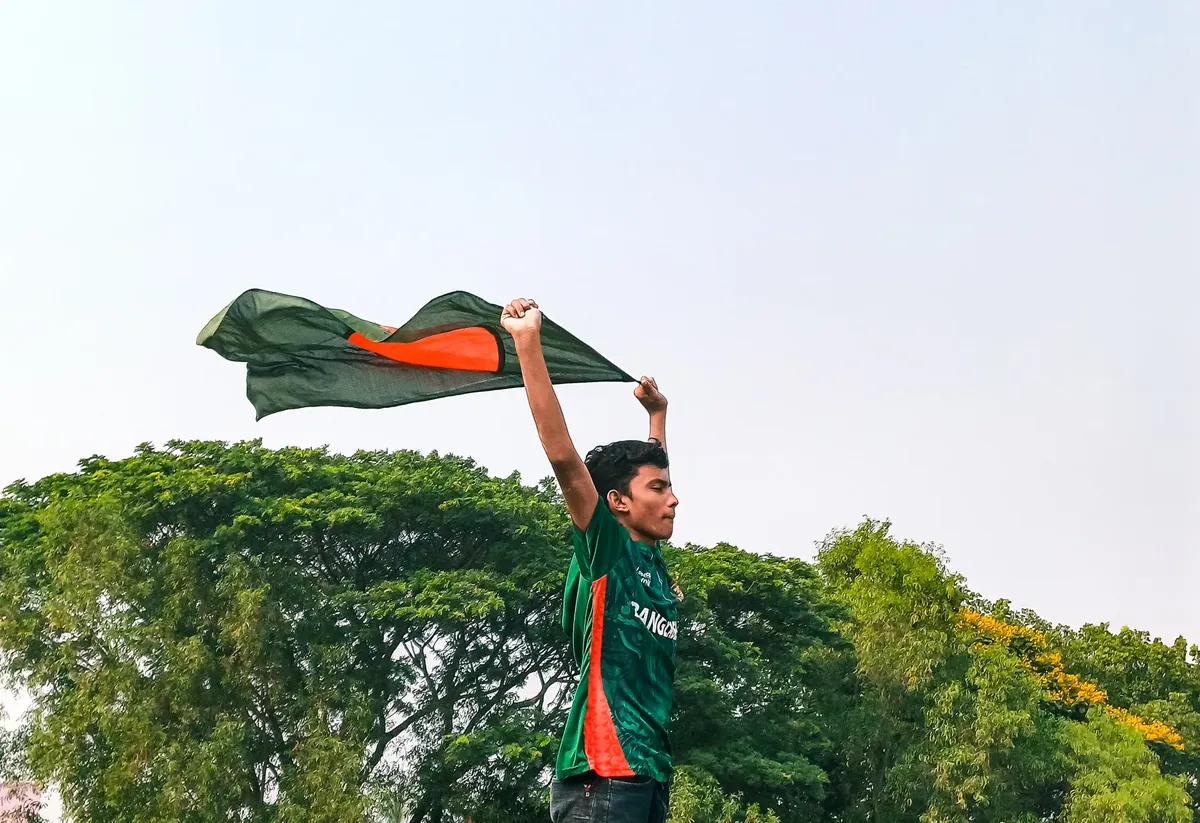A cricket fan passionately waving the Bangladesh flag outdoors under a clear sky, symbolizing national pride.